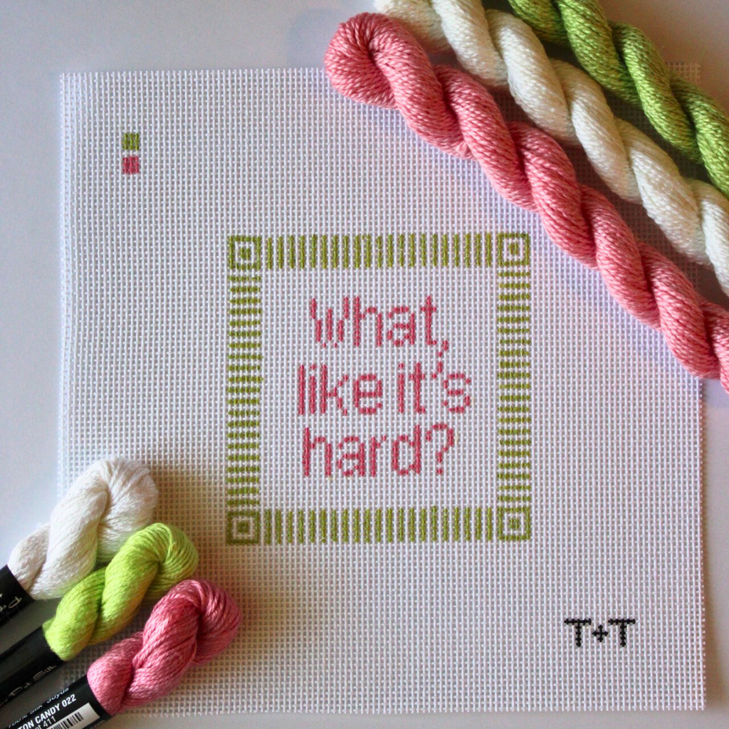 Threaded & Tipsy hand-painted needlepoint canvas featuring the phrase “what, like it’s hard?” in pink lettering, centered within a green geometric border. The initials "T+T" are painted in black in the bottom right corner. Three skeins of Threaded & Tipsy