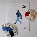 Threaded & Tipsy hand-painted needlepoint canvas featuring a pixel-style figure of a man walking while holding a phone to his ear, dressed in a black cap, black hoodie, blue jeans, and a blue and black jacket with red “RM” lettering. A painted color guide
