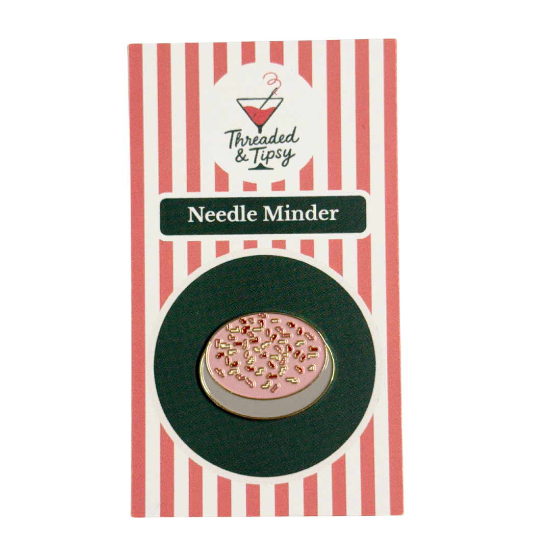 Pink needle minder with gold accents on a striped packaging by Threaded & Tipsy