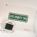 Needlepoint kit with 'US HWY 98' design on fabric, including thread labels and a swatch.