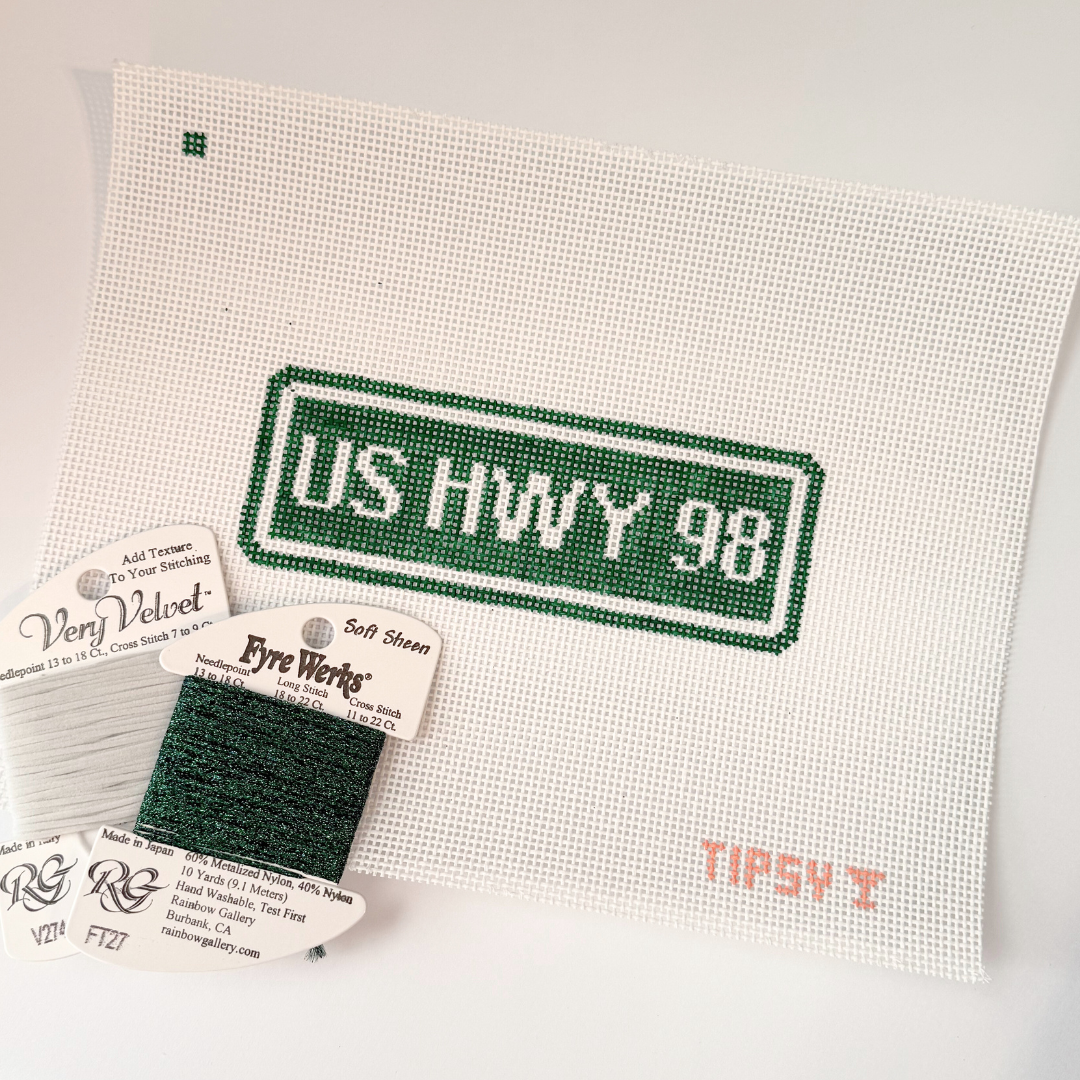 Needlepoint kit with 'US HWY 98' design on fabric, including thread labels and a swatch.