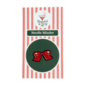 Red bow-shaped needle minder on green background with striped packaging