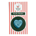 Heart-shaped needle minder with 'STITCH ME' text on a striped packaging