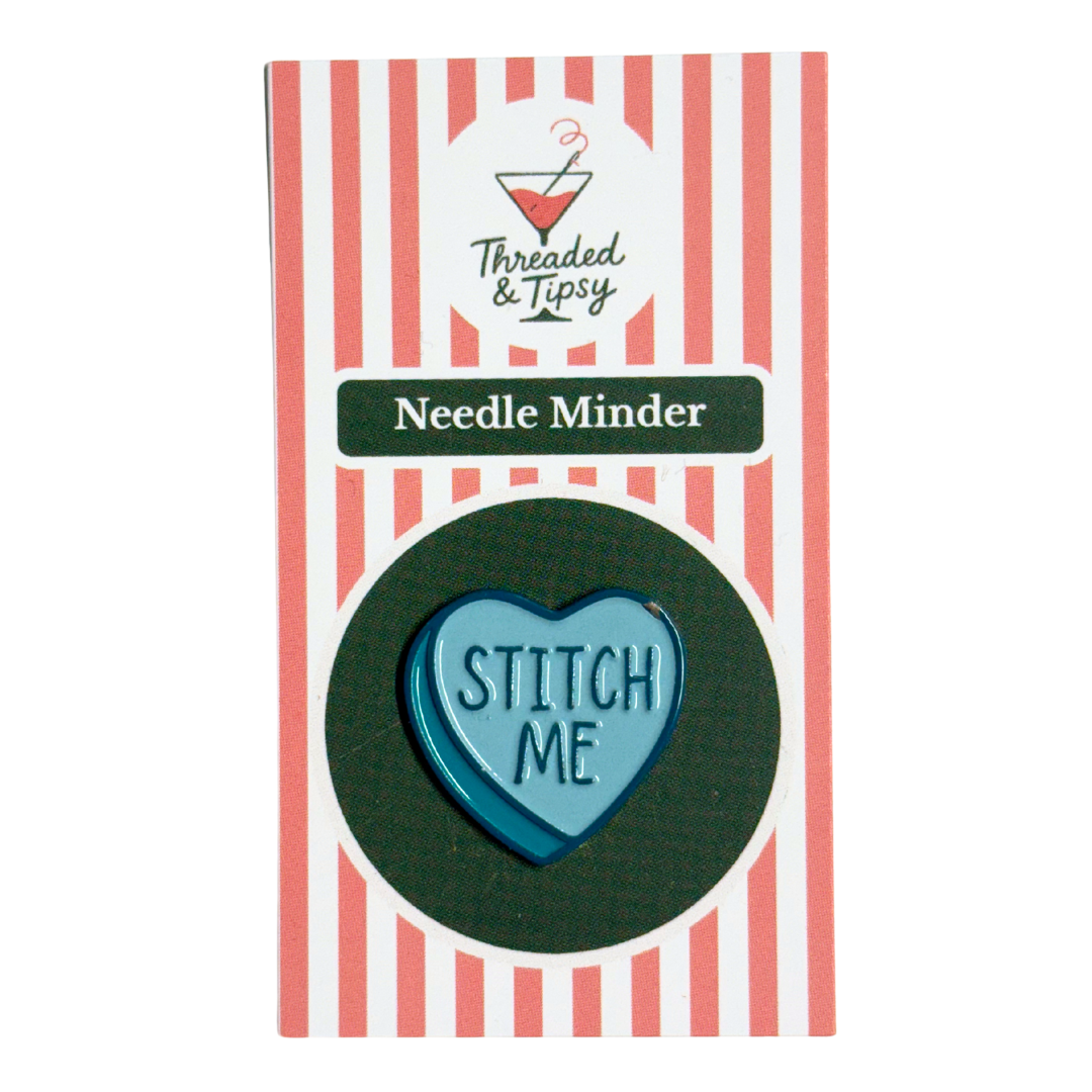 Heart-shaped needle minder with 'STITCH ME' text on a striped packaging